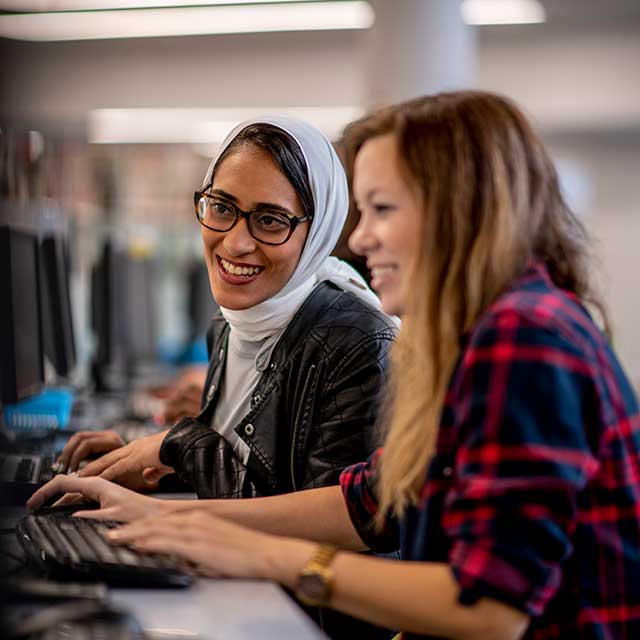 Two smiling women seated together using computers